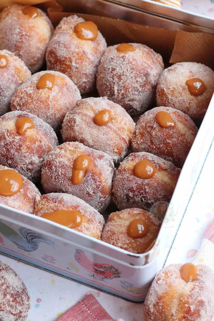 powdered sugar covered doughnuts in a tin with caramel sauce drizzled on them