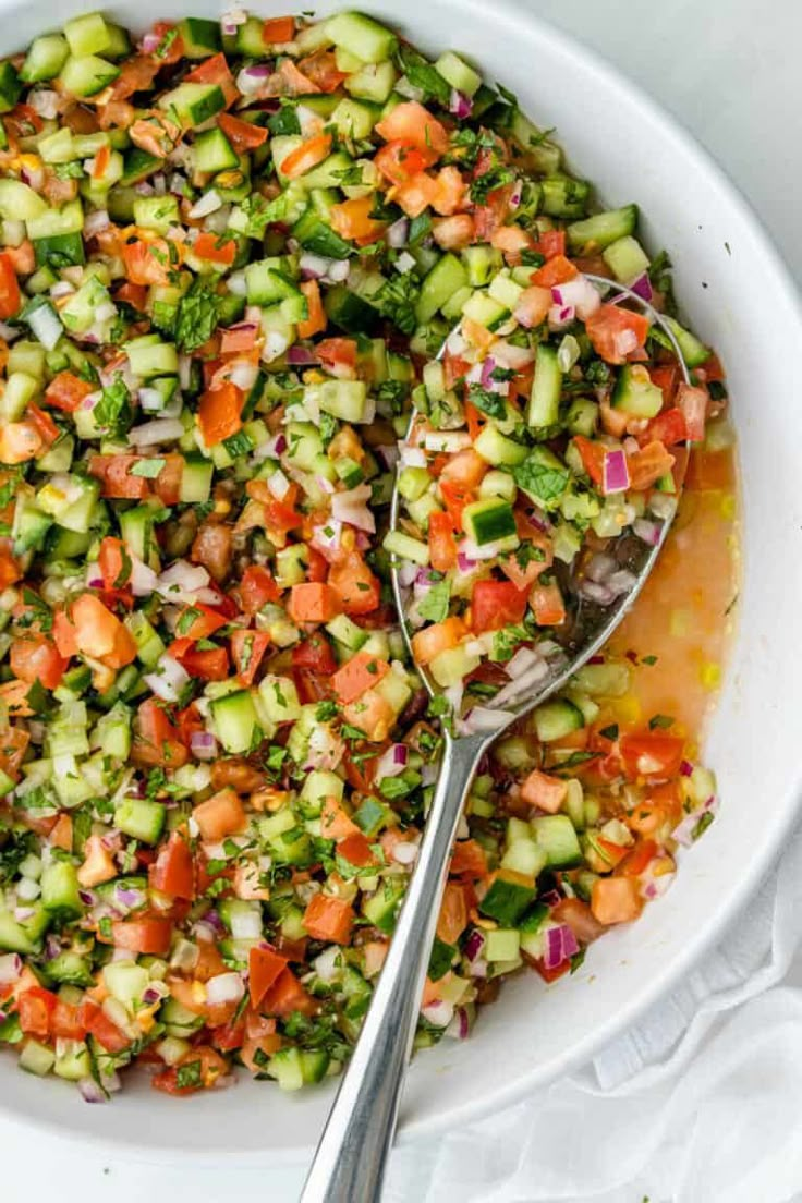 a white bowl filled with cucumber salad and two spoons on the side