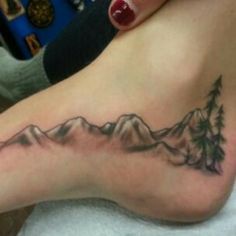 a woman's foot with mountains and trees tattoo on her left side ribcage