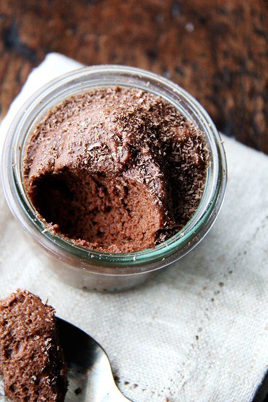 a glass jar filled with chocolate pudding sitting on top of a white napkin next to a spoon