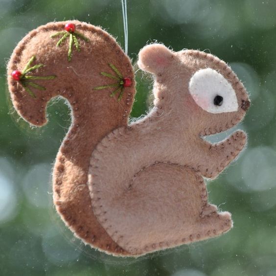 a felt squirrel ornament hanging from a tree branch with berries on it's tail