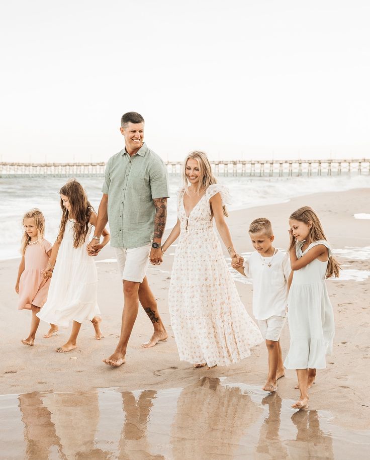 a family walking on the beach holding hands and smiling at the camera with their two children