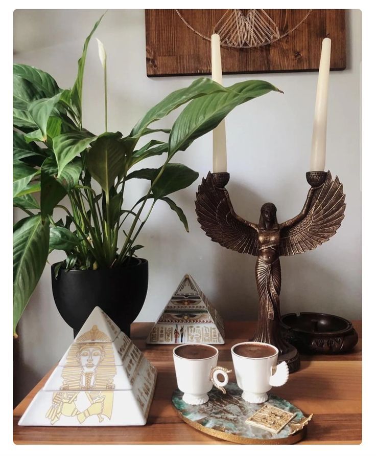 a table topped with two cups filled with coffee next to a plant and candle holder