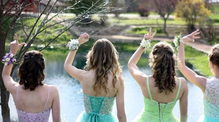 four young women in dresses are standing by the water with their hands up and arms raised