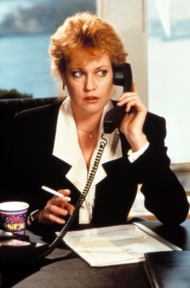 a woman sitting at a desk talking on the phone and holding a pen in her hand