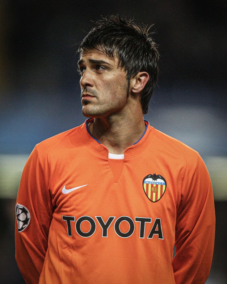 a soccer player in an orange shirt looking off to the side