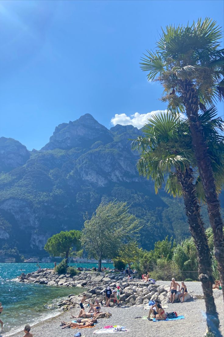 people are sitting on the beach and swimming in the water next to some mountain peaks