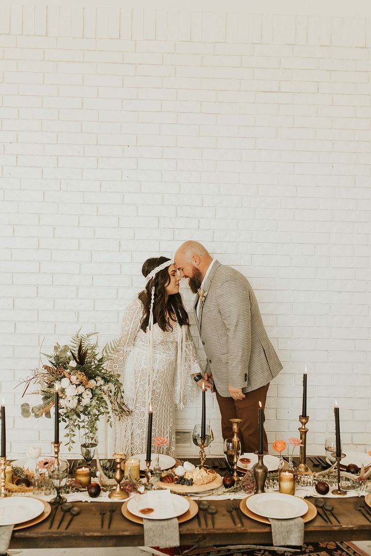 a bride and groom kissing in front of a table set with candles, plates and flowers