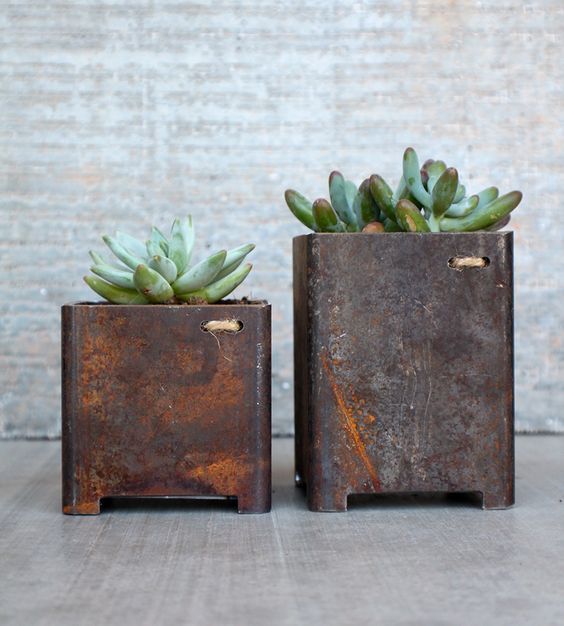 two metal planters with succulents in them sitting on a table next to each other