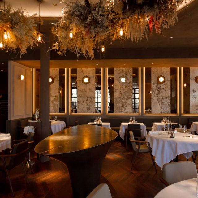 an empty restaurant with tables and chairs covered in white tablecloths, decorated with hanging plants