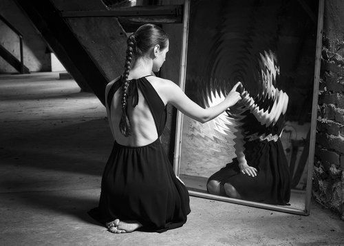 a woman sitting on the ground in front of a mirror with an angel painting behind her