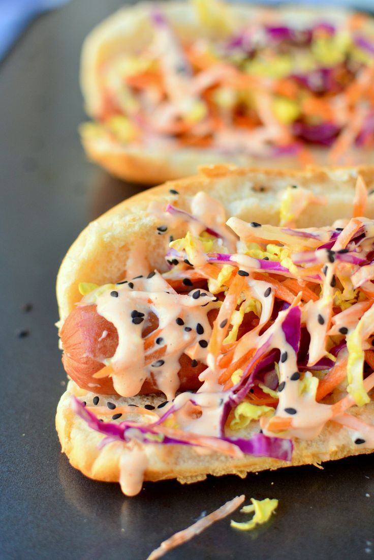 two hot dogs covered in toppings sitting on top of a black table next to each other