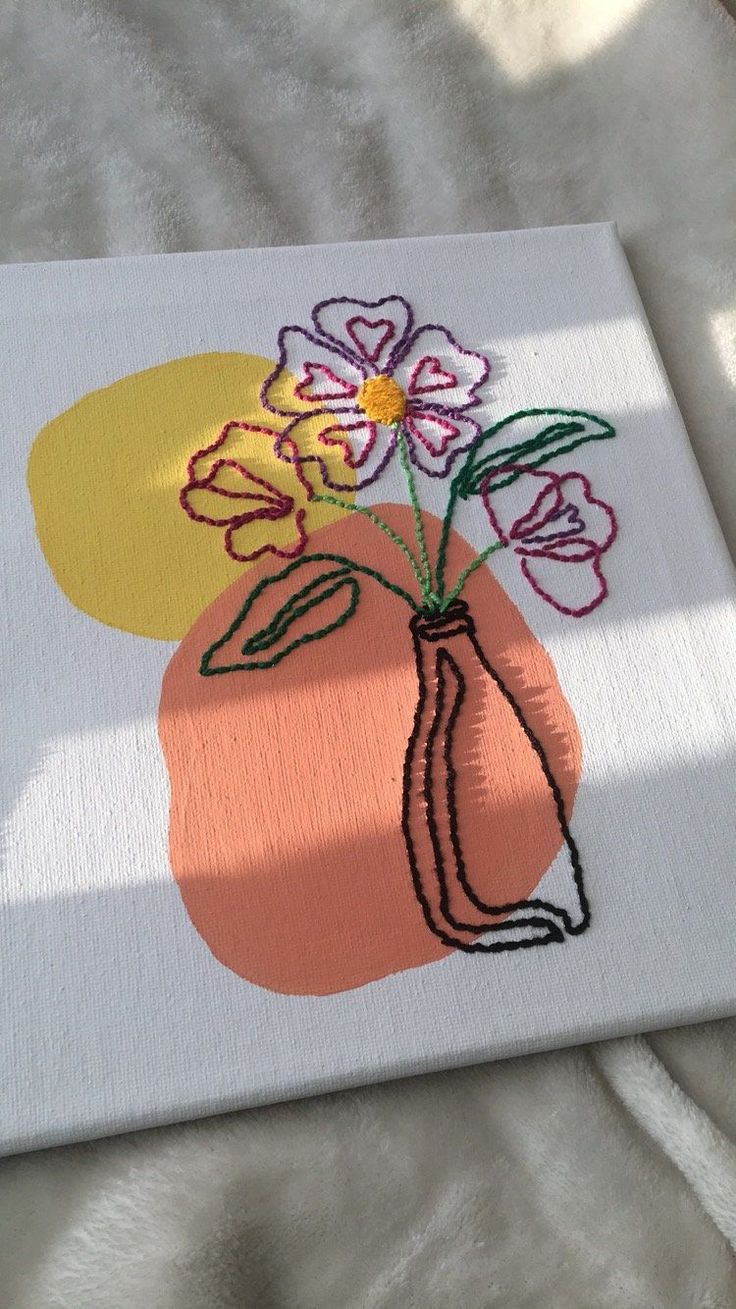 an orange vase with flowers is on a white surface and has been embroidered onto it