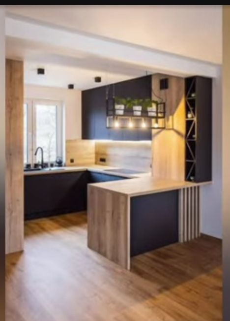 an empty kitchen with wooden floors and black cabinets in the center is lit by recessed lights