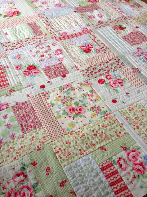 a quilted table topper with pink flowers and green squares on it, sitting on a wooden surface