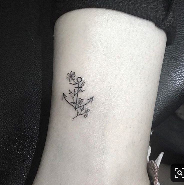 a small tattoo on the ankle of a woman's foot with an anchor and flowers