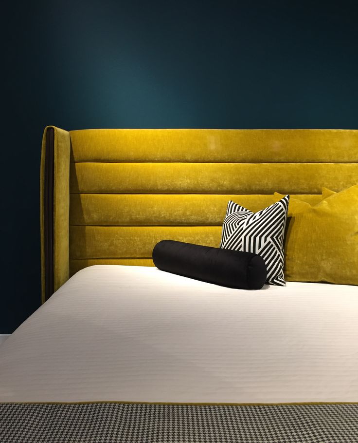 a bed with yellow velvet headboard and two black pillows on top of it, against a blue wall