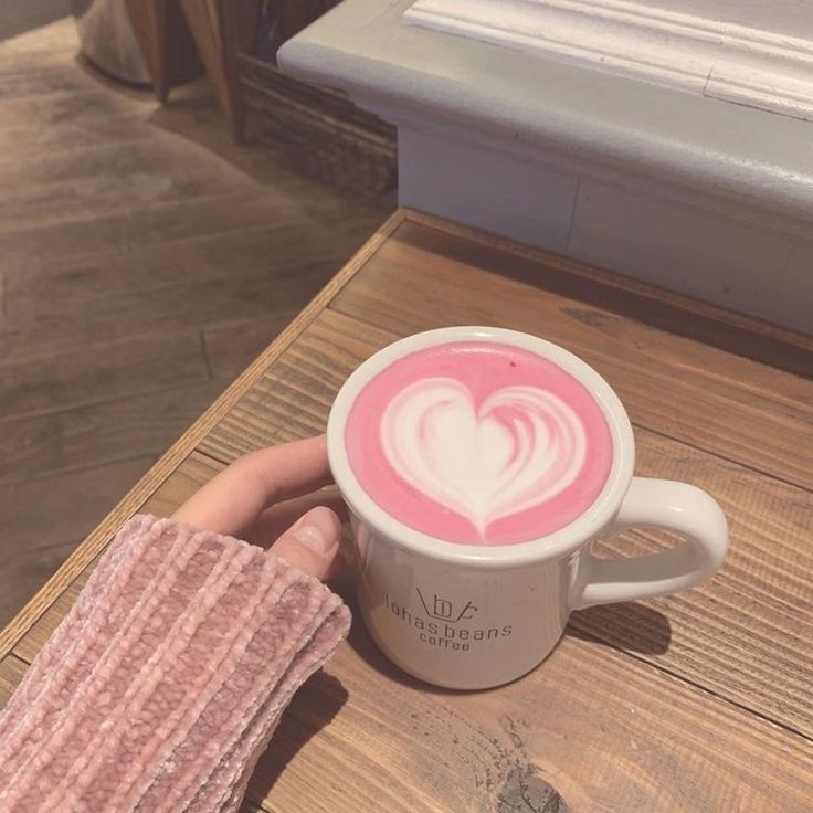 a person holding a cup of coffee with pink liquid in the shape of a heart