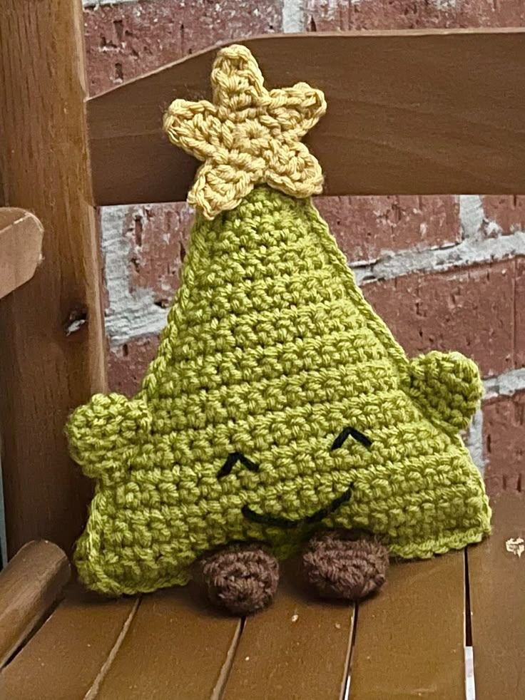 a green crocheted stuffed animal sitting on top of a wooden bench next to a brick wall