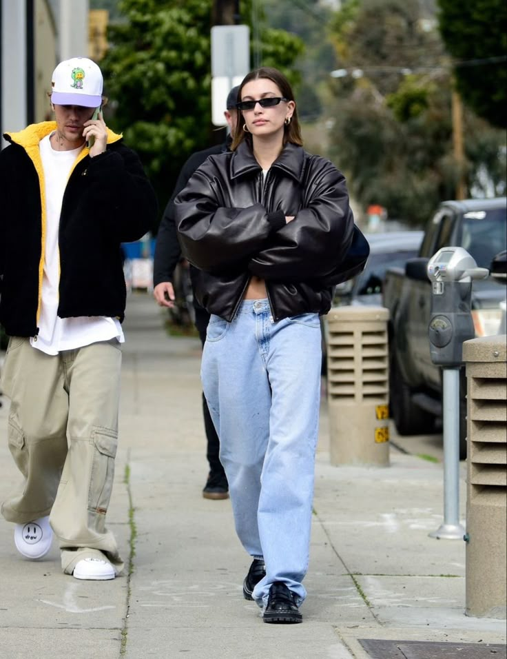 two people walking down the street with their arms crossed and one is wearing a black leather jacket