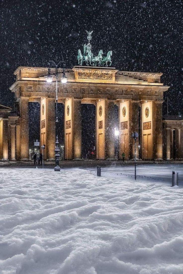 a snowy night in front of a large building with statues on it's sides