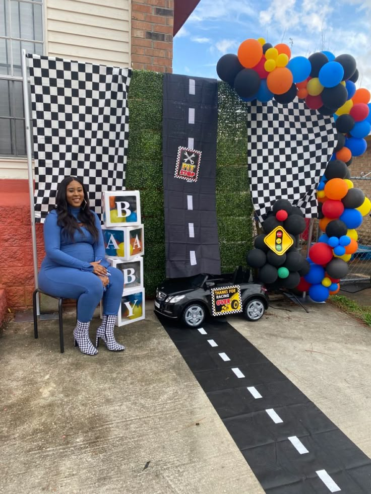 a woman sitting on a chair in front of a balloon arch with cars and balloons