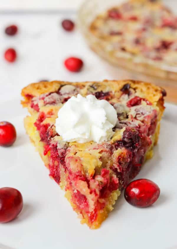 a slice of cranberry pie on a plate with whipped cream and cherries around it