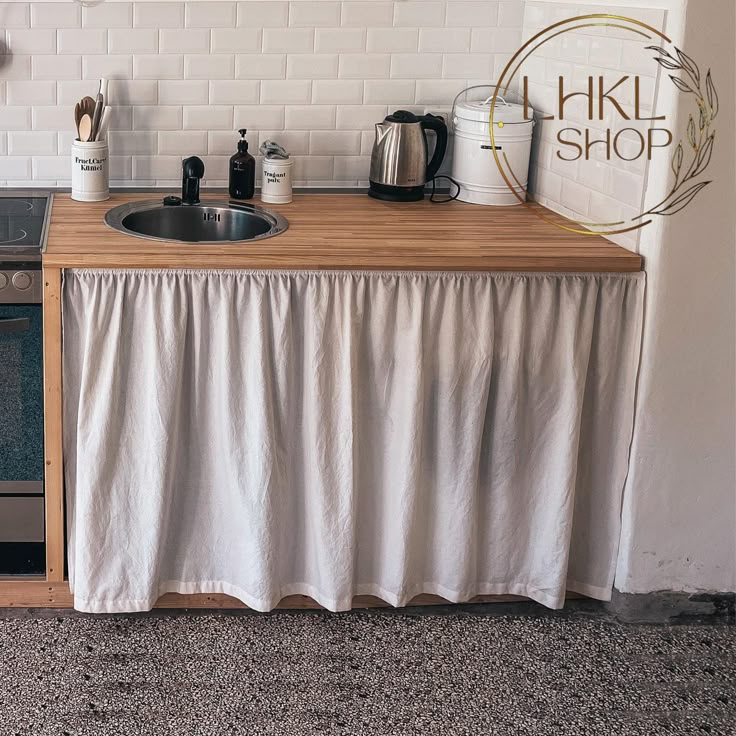 a kitchen with a sink, stove and counter top covered by a white curtain that is hanging on the wall