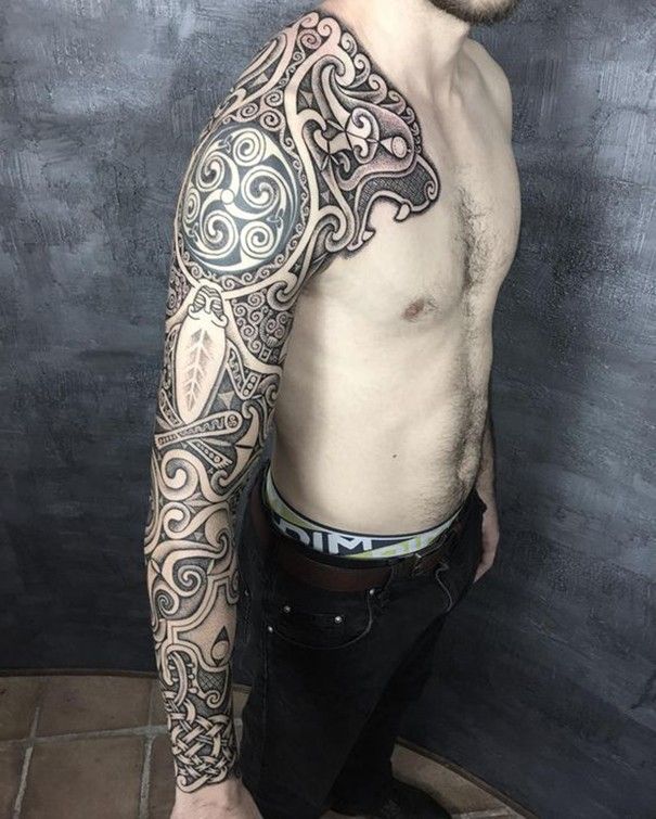 a man with a tattoo on his arm and chest standing in front of a wall