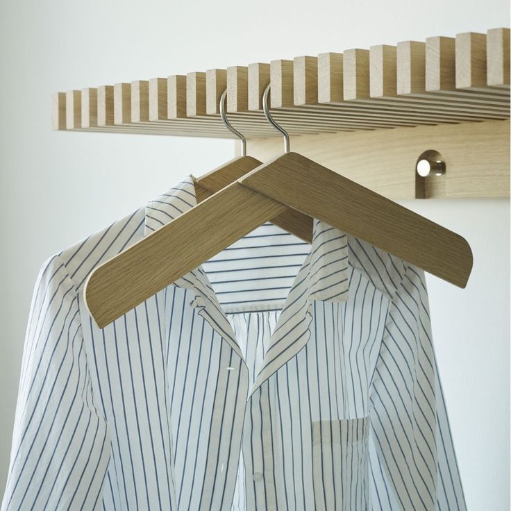 a shirt hanging on a wooden hanger next to a white wall with a striped shirt