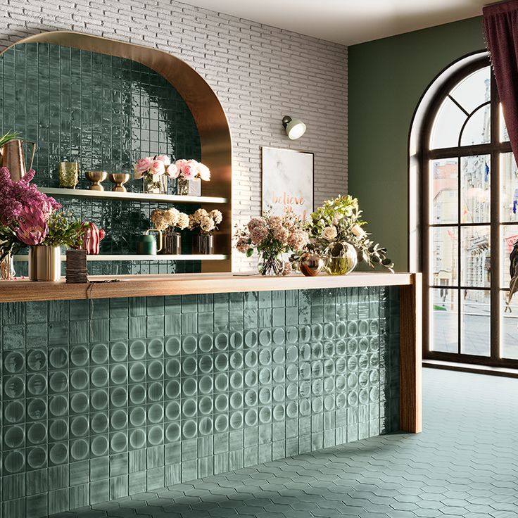 a green tiled bar with vases and flowers on the counter in front of an arched window