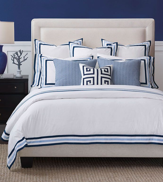 a bed with blue and white pillows in a bedroom next to a night stand on a rug