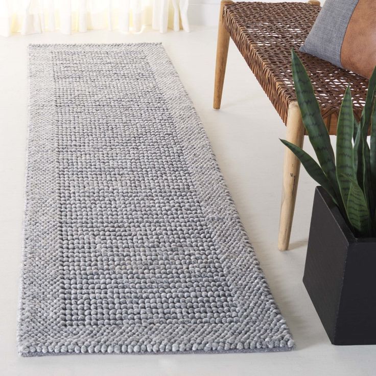 a gray rug sitting on top of a white floor next to a chair and potted plant