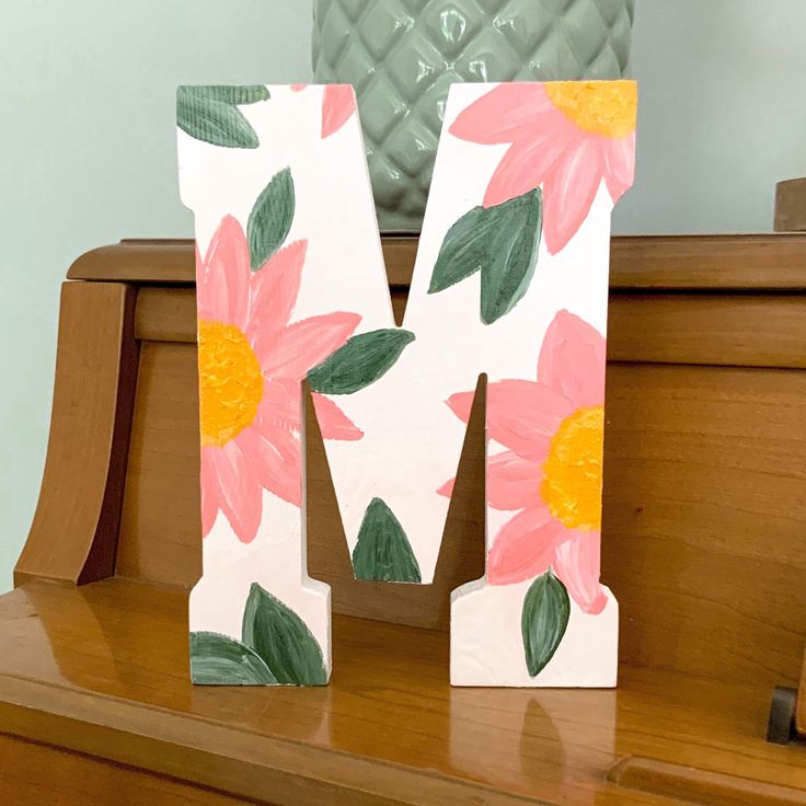 the letter m is painted with flowers on it's sides and sits on top of a piano