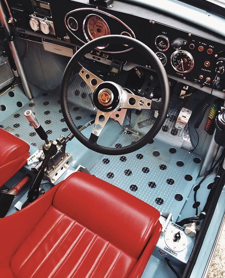 the interior of an old car with red leather seats and steering wheel, including two pedals