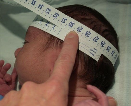 a baby being measured with a measuring tape on it's head by a hand