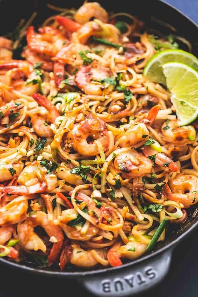 a skillet filled with shrimp, noodles and cilantro sauce next to a lime wedge