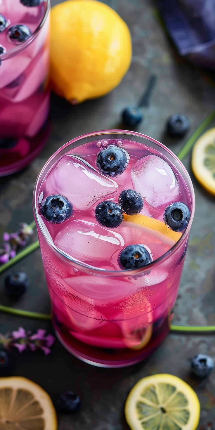 two glasses filled with blueberries and lemonade on top of a table next to sliced lemons