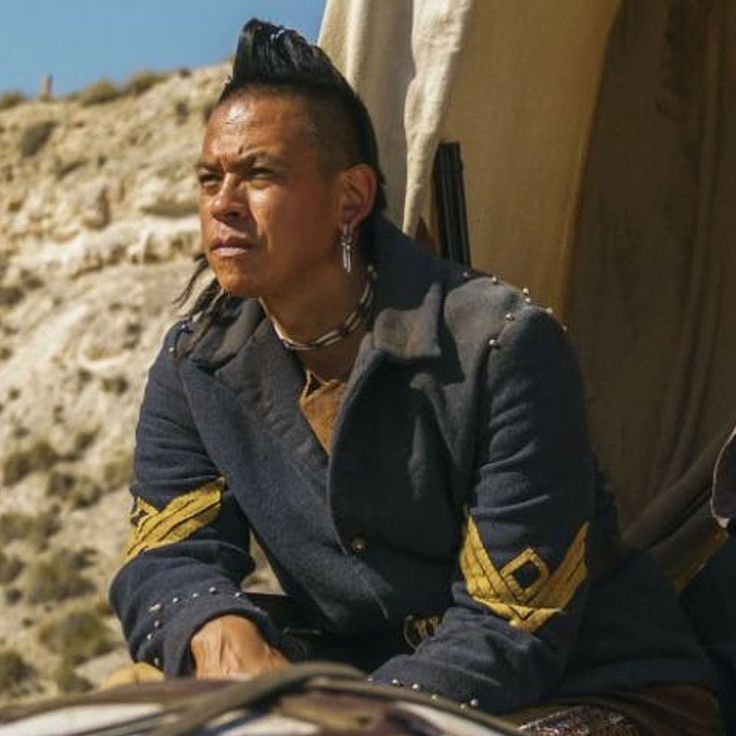 a man sitting on top of a chair next to a desert area with mountains in the background