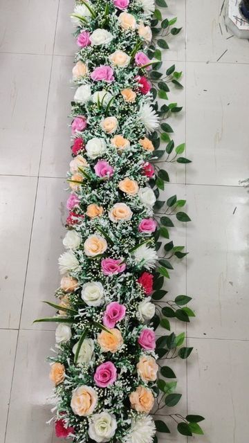 an arrangement of flowers arranged on the floor in a long line with greenery around it