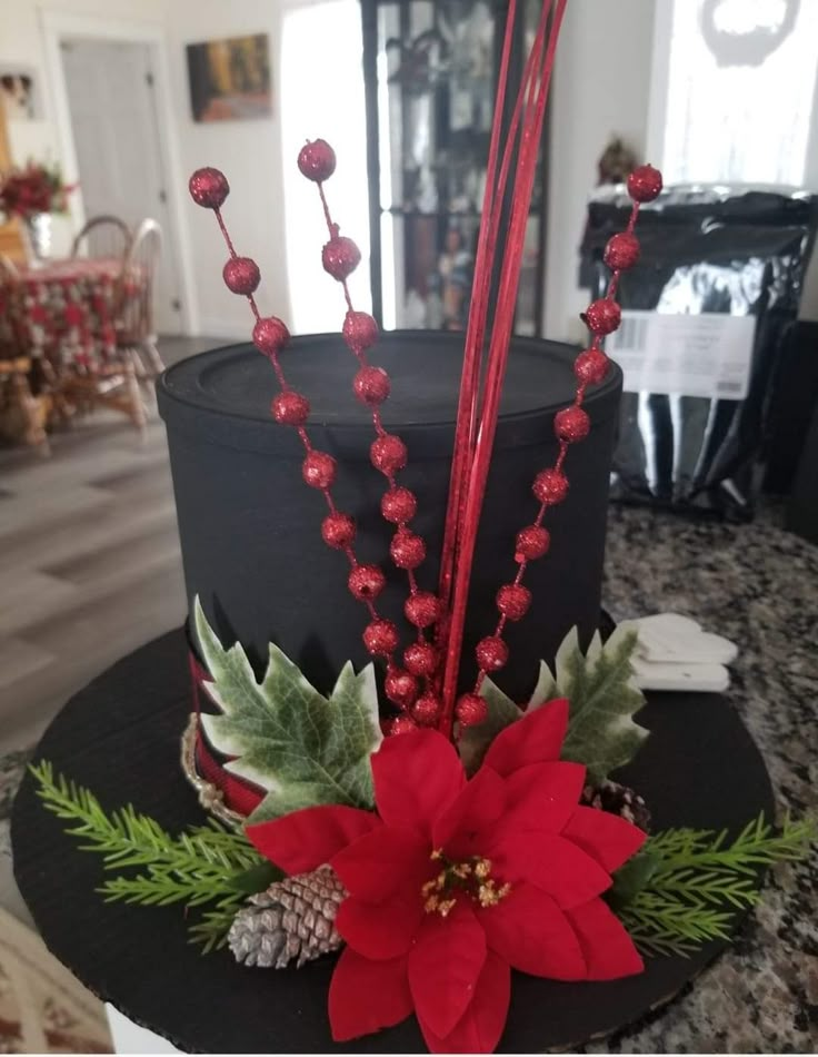 a black hat with poinsettis and greenery on the top is sitting on a table