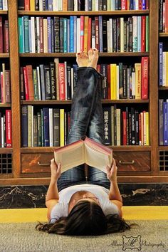 a woman laying on the floor reading a book in front of a bookshelf