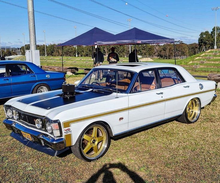 an old car is parked on the grass near other cars and people are looking at it