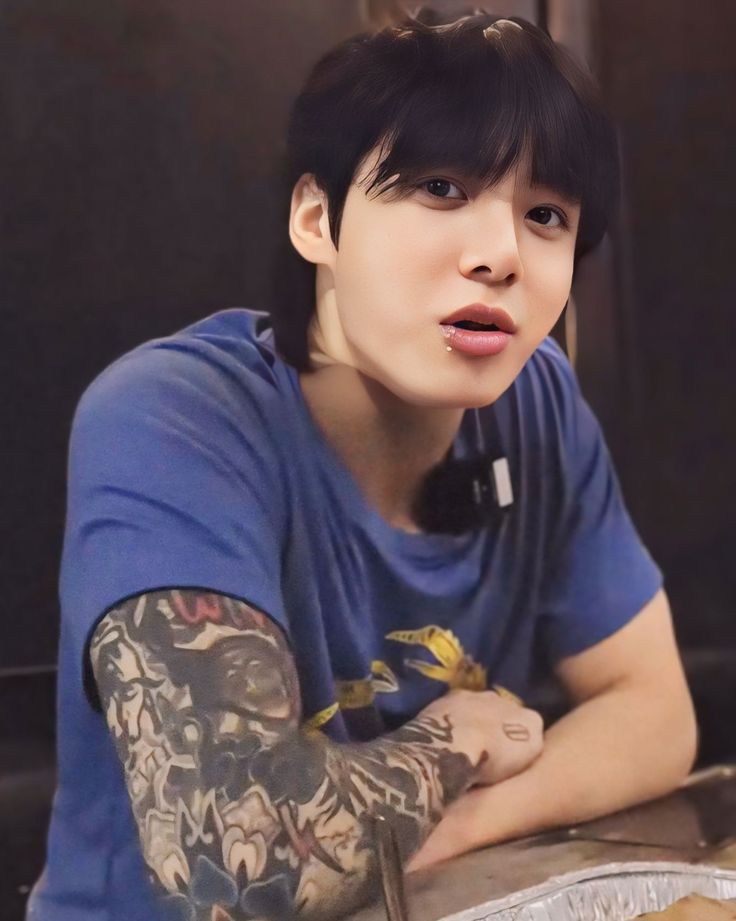 a young man with tattoos sitting at a table in front of a plate of food