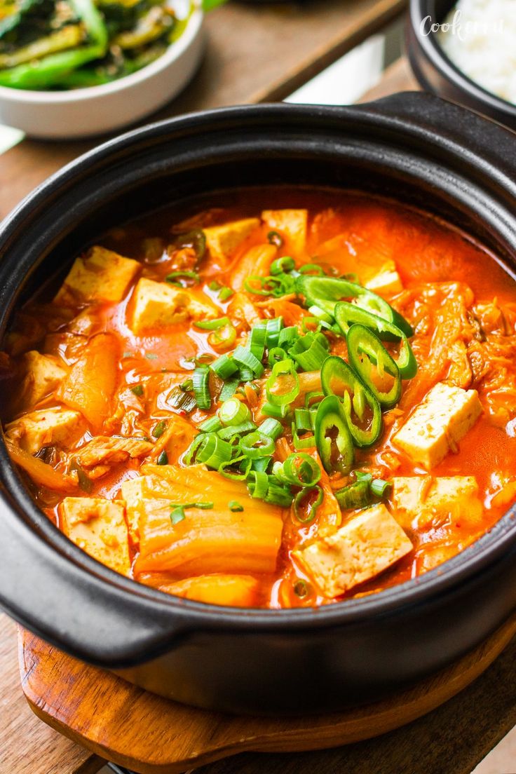 there is a bowl of soup with tofu and green onions in it on the table