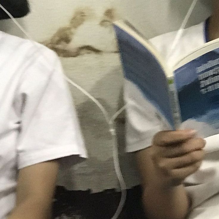 two people sitting on a bed with headphones in their ears and one reading a book