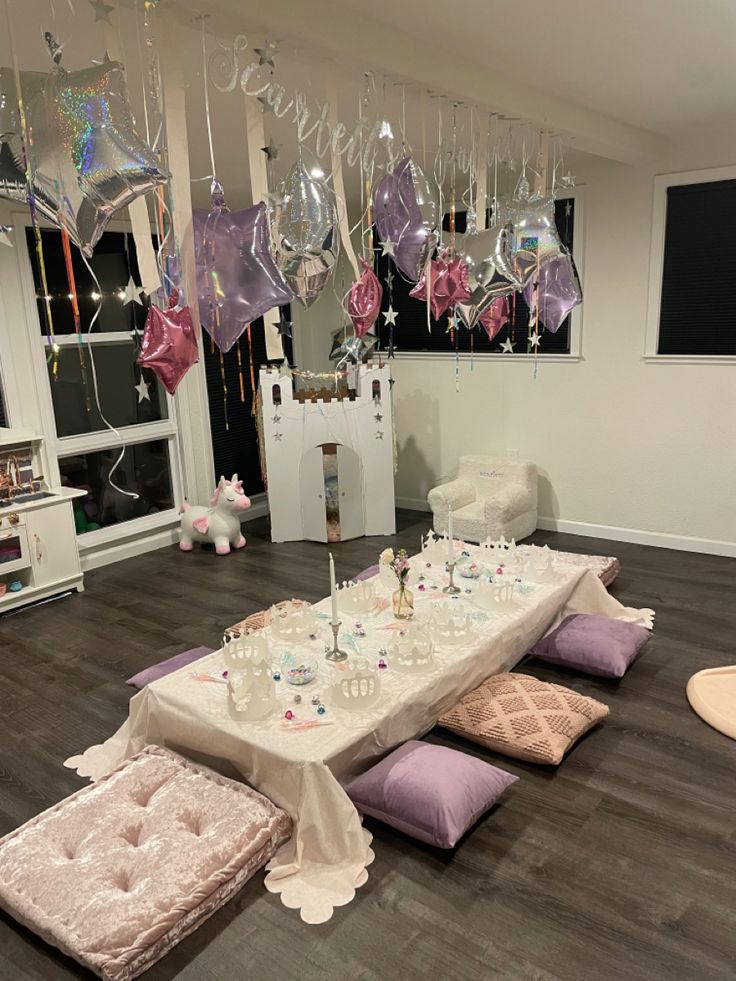 a table set up for a party with pink and purple balloons hanging from the ceiling