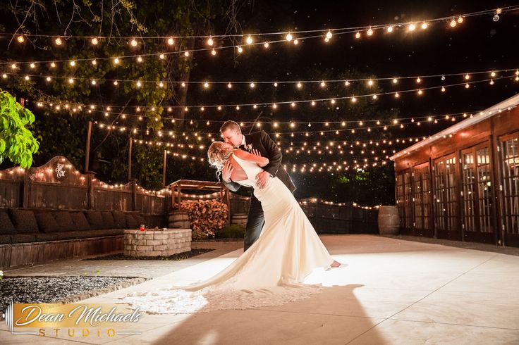 a bride and groom dance under string lights