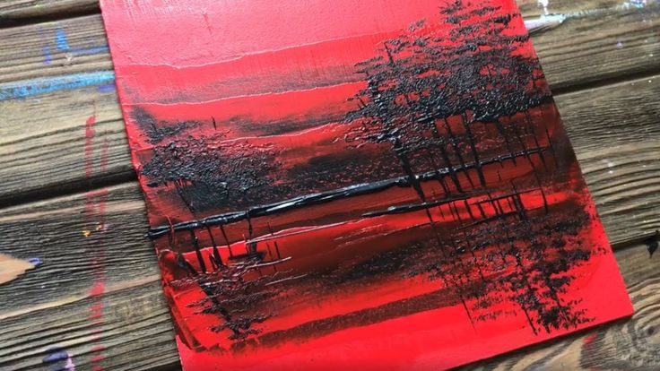 a red painting with black trees on it sitting on top of a wooden table next to scissors