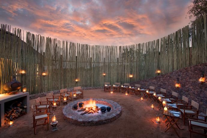 an outdoor fire pit surrounded by chairs and tables with lit candles on the table in front of it